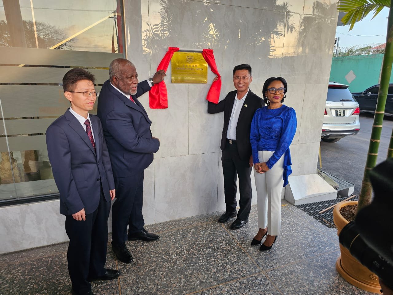 Members of the Royal Orchid Hotel and the Guyana Tourism Minister and Prime Minister take a photo by a plaque in front of the hotel.