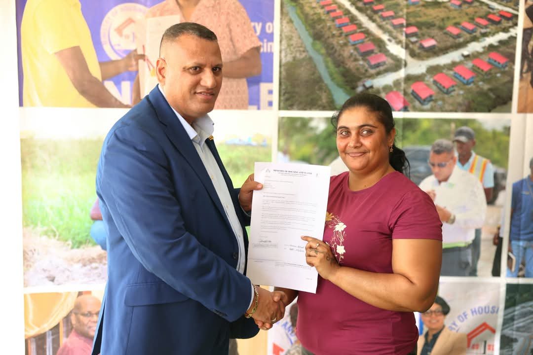 Housing and Water Minister Collin Croal presents an Agreement of Sale to a resident